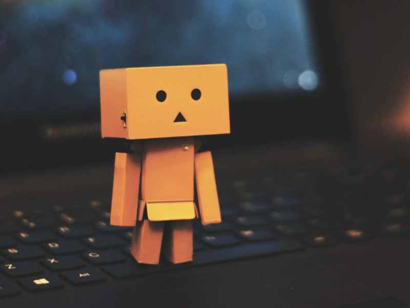 Cute little cardboard robot stands on top of a laptop keyboard